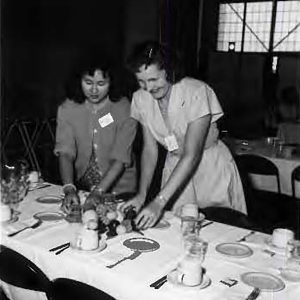 Two women prepare lunch table.