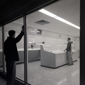 Man watches from outside two test operators in control room