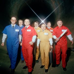 Members of AWT team in jumpsuits superimposed of interior shot of the tunnel.