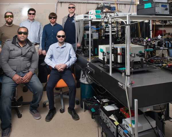 Six NASA scientists wearing laser safety goggles posing in a laboratory