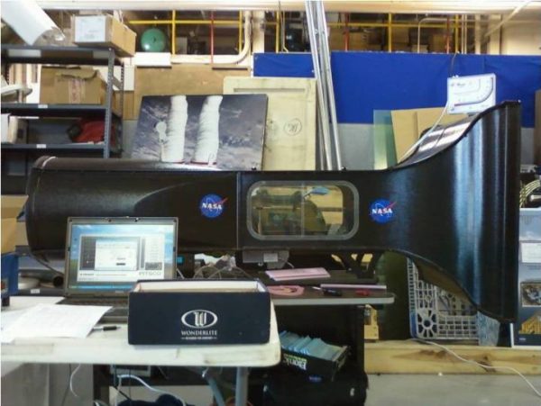 Small NASA wind tunnel inside a room with other objects surrounding it.